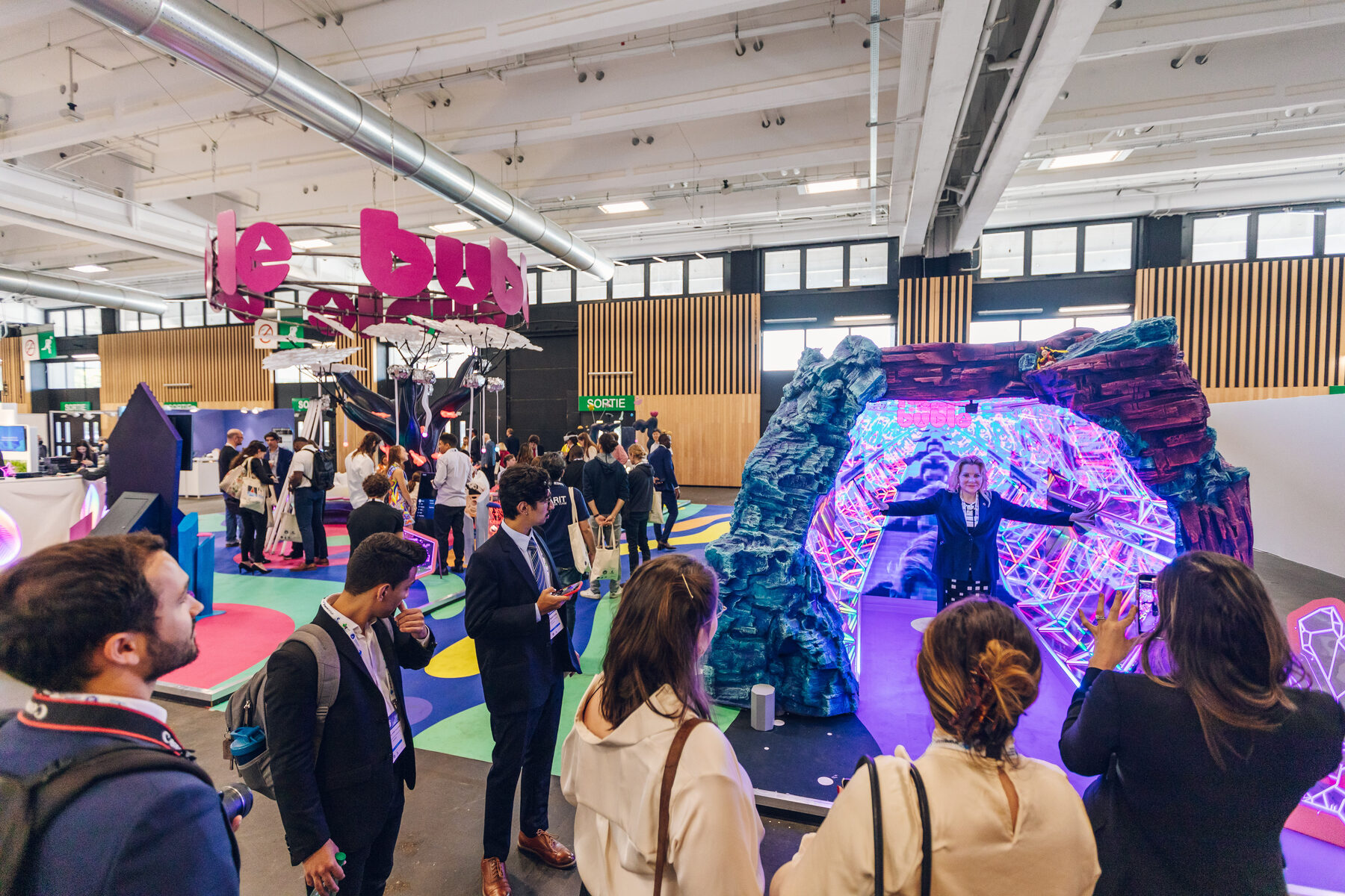 A crowd of delegates gathered at the rocky mouth of the Infinity Cave, watching a visitor inside the mirrored corridor.