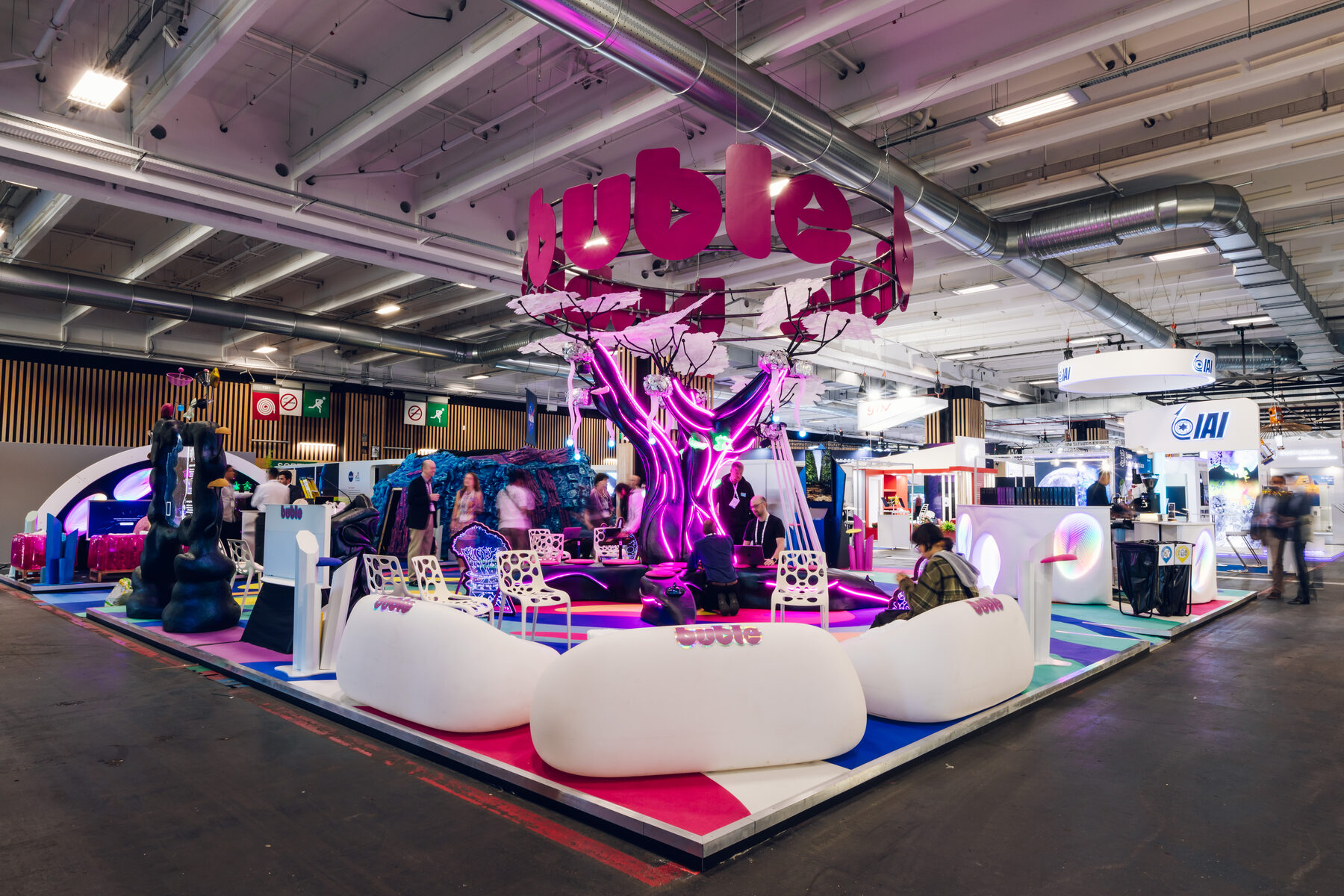 The full Buble Studios stand at IAC Paris — the glowing alien tree rising over white organic seating and a colourful floor, the pink buble sign overhead.