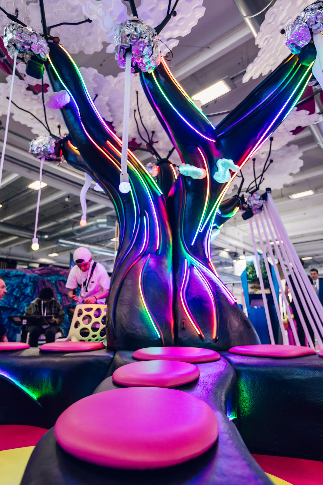 The four-metre Alien Tree on the Buble Studios stand — a twisting purple trunk edged in glowing LED lines, a pale swaying canopy overhead, and pink pebble seats around its roots.