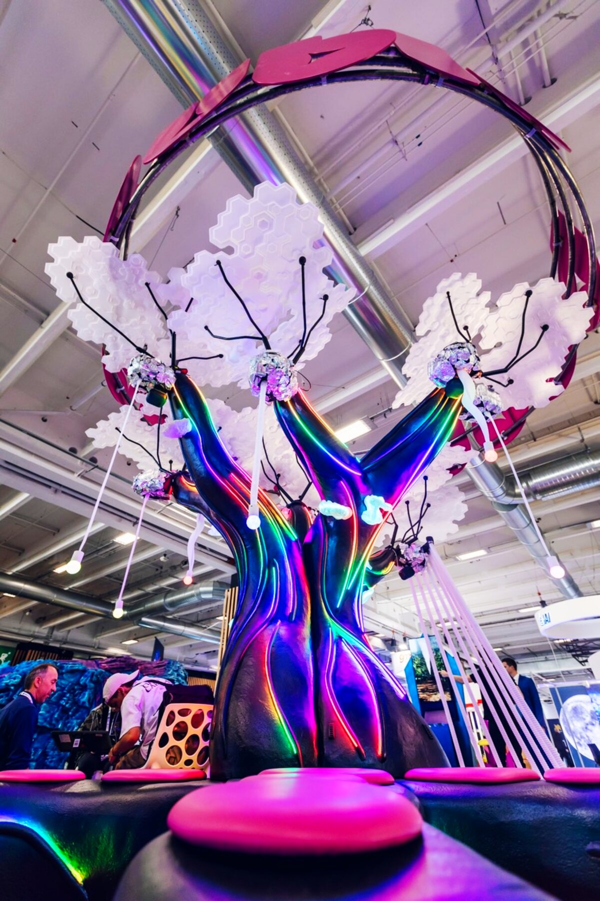 A sculptural, faceted tree wrapped in colour-shifting RGB light under an illuminated arch, glowing in a darkened venue.