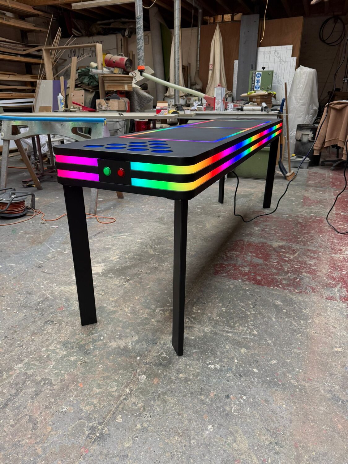 A single finished table from the side, black top and glowing rainbow edge bands, buttons visible on the end panel.