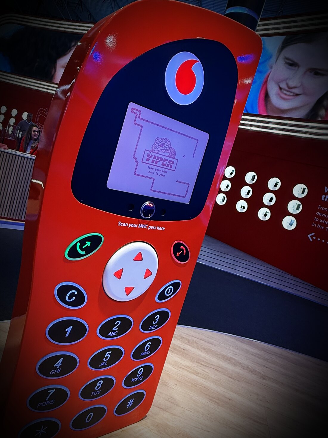 A giant red retro mobile phone with a backlit keypad and a colour screen running a playable game of Snake, on an exhibition stand at Mobile World Congress.