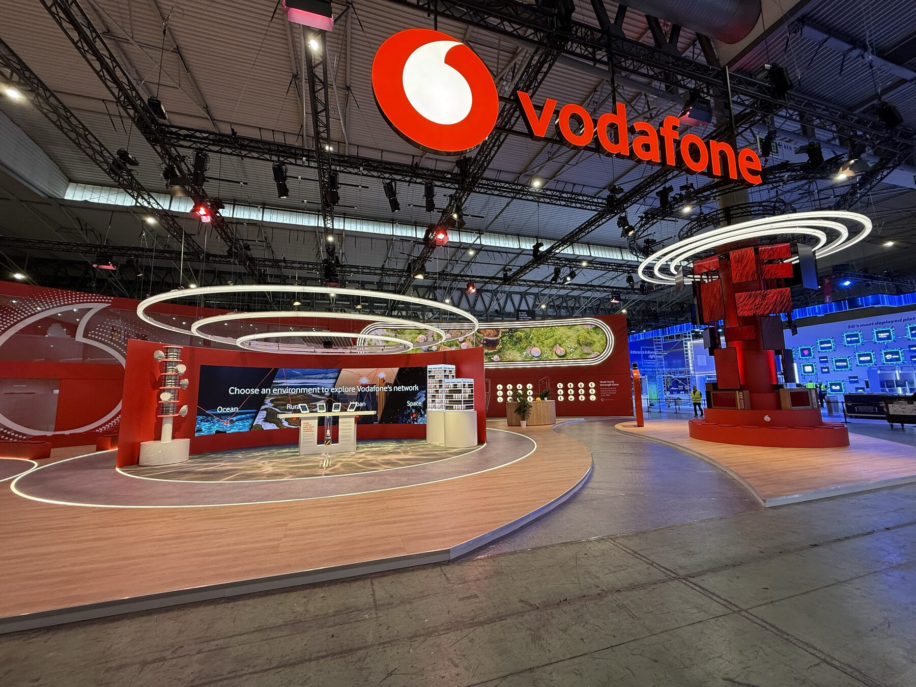 Wide view of the Vodafone stand before doors — the giant Vodafone sign overhead, the Seabed to the Stars area with its light rings and curved wall on the left, and the tornado attractor on the right.